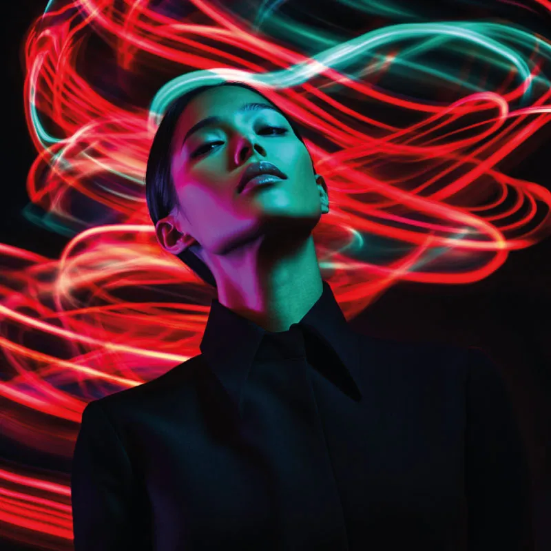 Retrato de una mujer de chaqueta negra rodeada de trazos de luz roja y verde